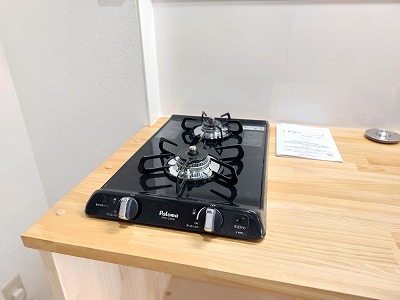おしゃれで機能的なキッチンは、天板を木で造作し、温かみとデザイン性をプラス。コンパクトですが、ちゃんと2口コンロとなっておりますので毎日の料理も便利に行うことができます。配置もシンプルでお手入れも楽々となるような設計です。木で造作をしていることにより木の温もりを感じるナチュラルな色合いが、空間にやさしさと落ち着きをもたらし、心地よい暮らしを演出します。