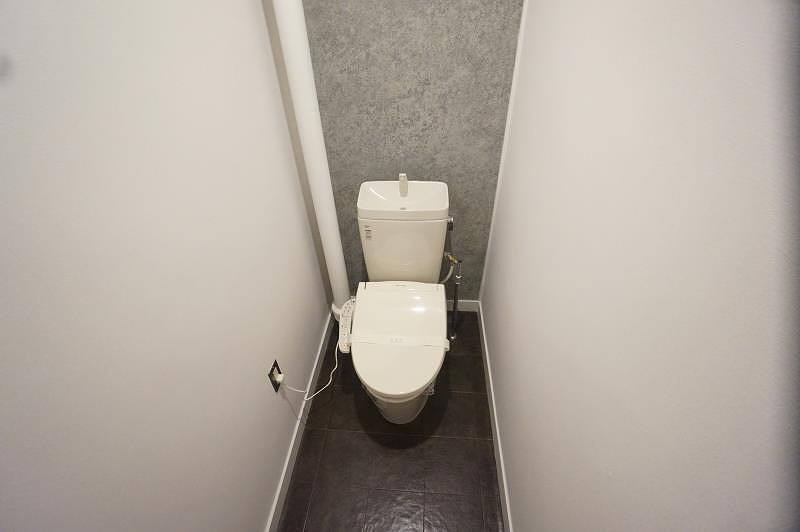 白く塗装された配管が空間にリズムを与え、グレーのアクセントクロスが落ち着きと上質さを添えるトイレ空間。シンプルながらも計算された配色と素材感のバランスが、日常のひとときを静かに引き立てます。無骨さと洗練を共存させたデザインは、コンパクトな空間だからこそ際立つ存在感。機能だけではない、居心地のよさと美意識が共鳴する、こだわりのトイレが完成しました。