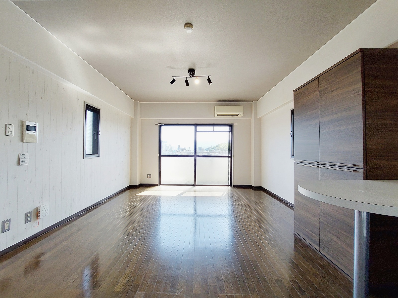 木目が美しいフローリングと落ち着きのある色合いでまとめられた、心地よい雰囲気のリビング。リフォームにより室内は全体的にすっきりと整い、無駄のないデザインが毎日の暮らしをより快適にしてくれます。大きな窓からたっぷり光が差し込み、室内をやさしく照らしてくれるため、日中は自然光だけでも気持ちよく過ごせます。天井のスポットライト風の照明がアクセントとなり、空間の表情を引き立ててくれる点も魅力です。